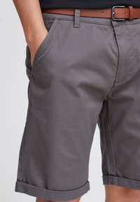 Graue Baumwollshorts mit glatter Textur, seitlichen Taschen, umgeschlagenen Säumen und einem braunen Leder-Gürtel. Einfaches Design mit klaren Linien.