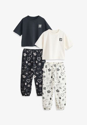 Dwa komplety casual piżam: jeden z czarnym crop topem i dopasowanymi czarnymi spodniami z białymi kwiatowymi i sercowymi wzorami, drugi z białym crop topem i dopasowanymi białymi spodniami w wzory.