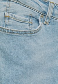 Ljusblå denimjeans med en stor bakficka, synliga sömmar och bälteshällor, som erbjuder en mjuk textur och en avslappnad design.