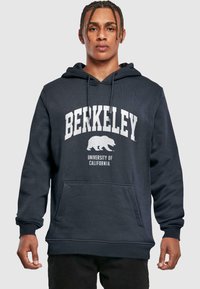 Tumed sinine kapuutsiga pluus, mis on valmistatud puuvillast segust. Ees on känguru tasku, valgete trükitud "BERKELEY" tekst ja karu logo rinnal.