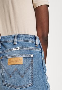 Ljusblå denimjeans med en läderpatch från "Wrangler", kontrasterande sömmar och två bakfickor med metallnitar.