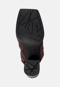 Sole of a black-heeled shoe with geometric tread patterns and a brown fabric upper part visible around the edges.