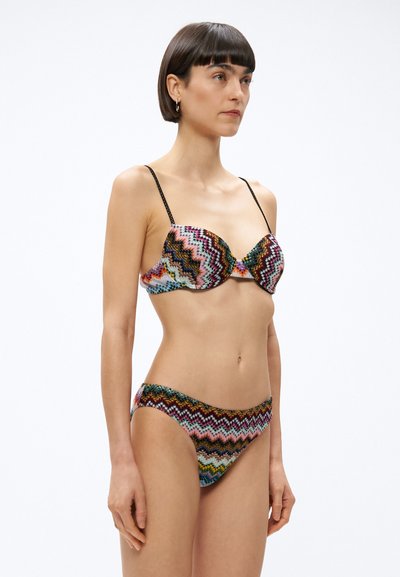 Ένα πολύχρωμο σετ μπικίνι με ζιγκ-ζαγκ μοτίβο. Το πάνω μέρος έχει διαμορφωμένα σουτιέν με λεπτές μαύρες τιράντες, ενώ το κάτω μέρος διαθέτει το �ίδιο σχέδιο ζιγκ-ζαγκ.