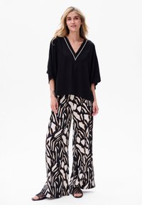 Schwarzes, lockeres Oberteil mit V-Ausschnitt und silbernem Trim, kombiniert mit weit geschnittenen Hosen im schwarz-weißen Tierdruck-Design.