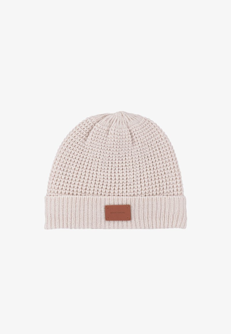 Gebreide beanie in lichtbeige met een gestructureerd weefpatroon, omgevouwen manchet en een rechthoekige leren patch met reliëfbranding aan de voorkant.