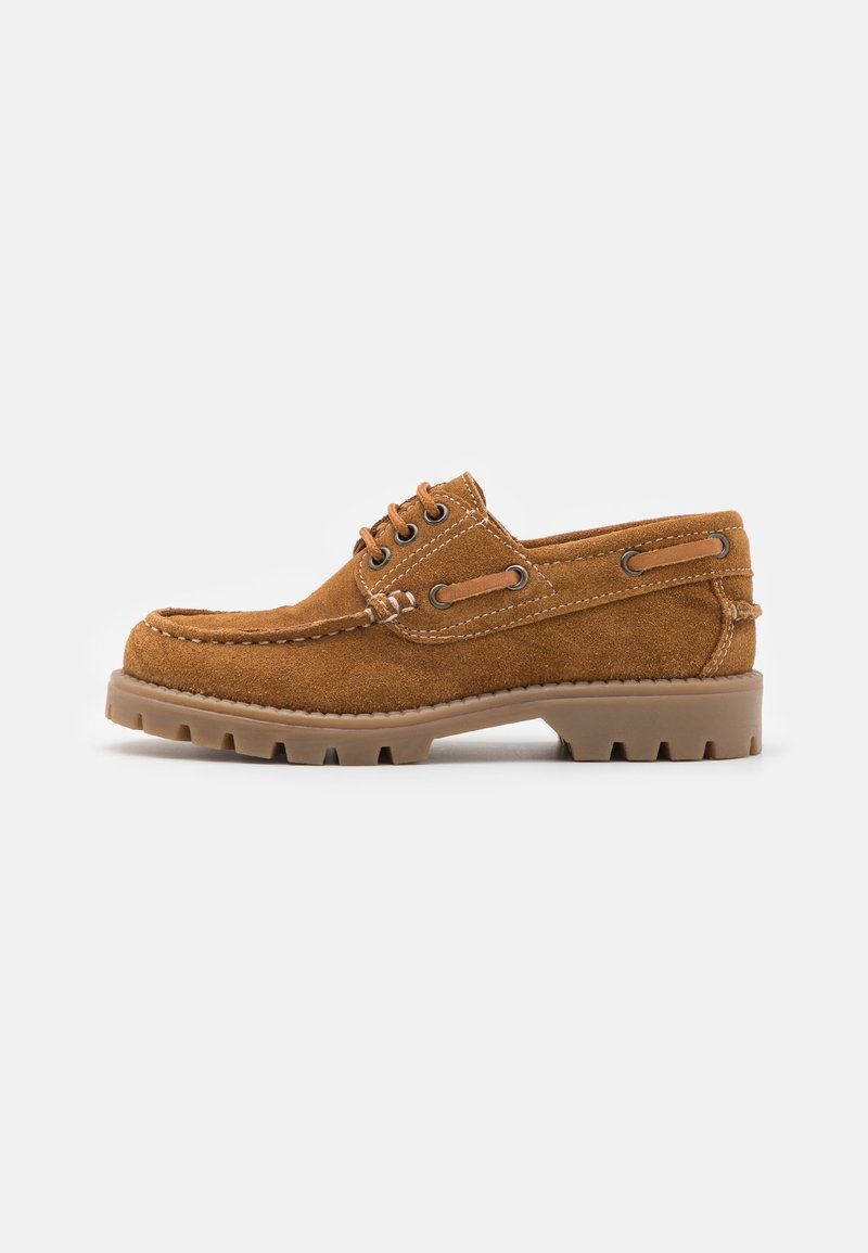 Chaussure bateau marron en daim à lacets avec une épaisse semelle en caoutchouc rainurée et des détails en cuir sur le côté, sur un fond blanc uni.