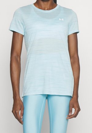 Kvinde iført lyseblå kortærmet Under Armour trøje og matchende lyseblå leggings, stående foran en ensfarvet hvid baggrund.