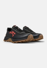 Scarpe da ginnastica nere con una superficie testurizzata, suole in gomma e lugs prominenti. Presentano un logo rosso e un robusto design con lacci.