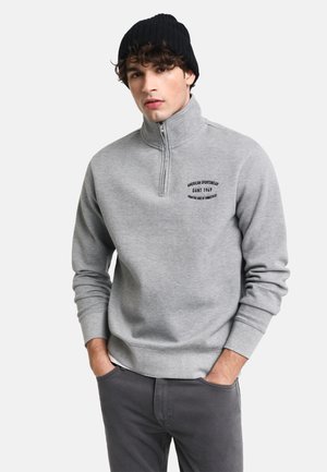 Gray zip-up sweatshirt featuring a high collar, ribbed cuffs, and an embroidered logo on the chest. Pair with dark gray pants.