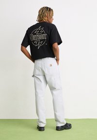 Zwart graphic t-shirt met het woord "Detroit" en een bliksemschichtontwerp, gecombineerd met lichtgrijze cargobroeken en zwarte sneakers.
