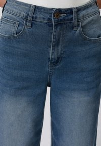 Denims i middels blå med en lett falmet finish. Funksjoner inkluderer knappelukking, beltesløyfer og standard lommeutforming.
