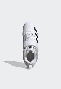 Zapatilla deportiva blanca con parte superior de malla texturizada, detalles en negro, una correa sobre los cordones y una etiqueta en el talón con marca.
