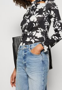 Zwarte longsleeve bodysuit met witte bloemenprint; hoge halslijn, slim fit. Lichtblauwe high-waisted jeans met zakken, casual stijl.