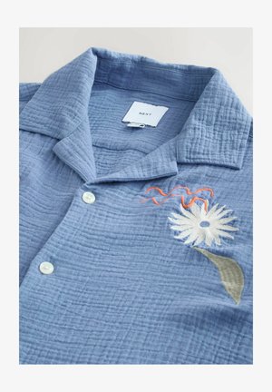 Hellblaues Hemd aus strukturiertem Stoff, mit einem Kentkragen, Knopfverschluss und floraler Stickerei in Weiß, Grün und Orange.