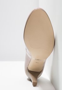 Chaussure à talons hauts avec une tige en cuir rose lisse, un bout pointu et un talon empilé texturé marron clair. Dispose d'une semelle en caoutchouc avec des rainures.