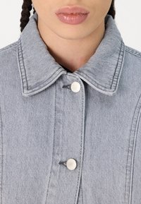 Veste en denim grise avec un col, boutons-pression argentés et un tissu texturé avec des coutures visibles.