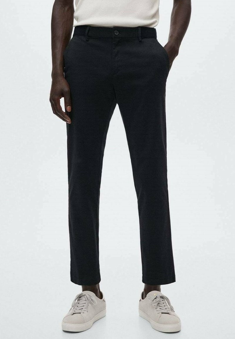Pantalon en coton noir à coupe droite, avec poches latérales et un seul bouton à l'avant. Associé à des baskets gris clair.