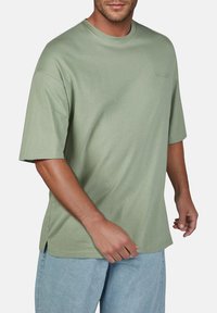T-shirt di cotone verde con collo a giro, maniche corte e vestibilità rilassata. Presenta fessure laterali all'orlo per un comfort maggiore.