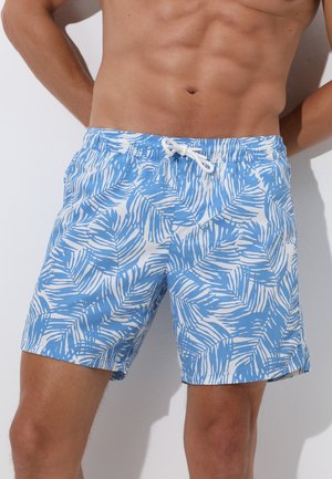 Torace e gambe maschili che indossano pantaloncini da bagno blu e bianchi con motivo a foglie e coulisse bianca annodata in vita.