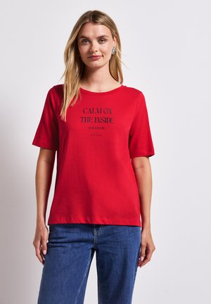 T-shirt rouge à manches courtes avec un col rond et un texte imprimé noir disant « CALME À L'INTÉRIEUR, CONCENTRÉ À L'EXTÉRIEUR. » Matériau en coton doux.