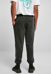 Sorte bomulds joggere med elastisk talje, baglomme og blåt grafisk detalje på siden. Båret med sorte ankelstøvler.