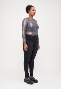 Long-sleeve sheer top with metallic leopard print pattern, paired with high-waisted black skinny jeans and chunky black platform shoes.