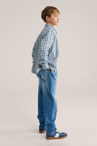 Blå- och vitrutig skjorta med knappar, avslappnade ljusblå jeans och marinblå sneakers med vita detaljer. Avslappnad outfit sedd från sidan.