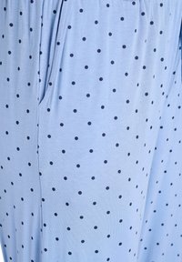 Gaiši zils audums ar tumši zilu punktiņu rakstu, ar brīvu piegriezumu un kabatām. Tekstūra izskatās gluda un maiga.