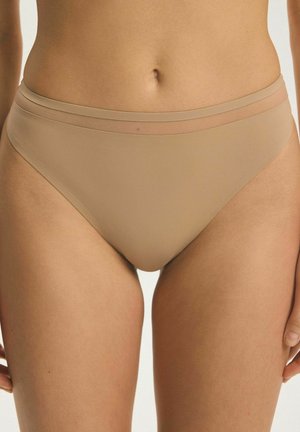 Žena v bezšvovej spodnej bielizni v odtieni nude v bikinovom štýle, zobrazená od pása po polovicu stehna na jednofarebnom pozadí.