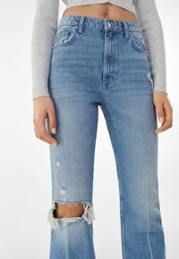 Ljusblå denimjeans med hög midja, slitna detaljer och fransade fållar. Tyget har en slät textur och en klassisk femficksdesign.