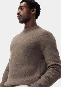 Brun ribbet striktrøje med rund hals og lange ærmer, lavet af blødt materiale, med et subtilt tekstureret mønster.