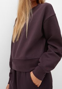 Felpa viola con scollo a girocollo, maniche lunghe e polsini a coste, caratterizzata da una vestibilità comoda e un piccolo dettaglio con logo sul polsino.