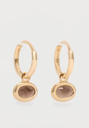 Boucles d'oreilles créoles en or avec des pierres précieuses en quartz fumé ovales serties dans des chatons en or lisse, présentant un texte de marque gravé subtilement à l'intérieur des créoles.