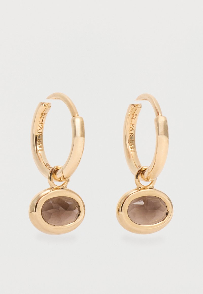 Κρίκοι σκουλαρίκια από χρυσό με οβάλ πολύτιμους λίθους καπνίτη χαλαζία, τοποθετημένους σε λείες χρυσές ζώνες, με διακριτικό χαραγμένο κείμενο της μάρκας στο εσωτερικό των κρίκων.