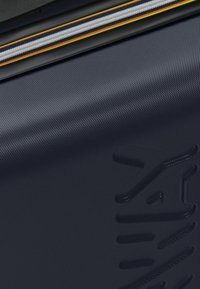 Harde koffer in donker marineblauw met een gestructureerde afwerking, voorzien van een contrasterende rits met gekleurde accenten en een reliëflogo-detail.