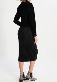 Schwarze Cordjacke mit tailliertem Schnitt, kombiniert mit einem schwarzen gerippten Midirock und Ankle Boots mit Leopardenmuster.