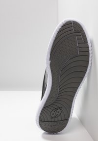 Suela de zapatilla deportiva negra con una superficie de goma gris texturizada; contorneada en blanco con un patrón de olas y un logotipo.