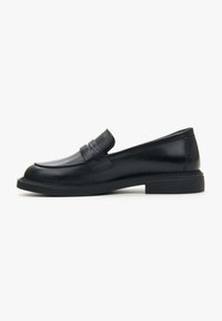 Zwarte leren instappers met een gladde afwerking, voorzien van een decoratieve riem en contrasterende stiksels op een lage, platte rubberen zool.