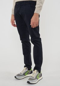 Pantaloni in velluto a coste blu navy con vestibilità slim, tasche laterali e trama sottile, abbinati a sneaker sportive grigie e verdi.