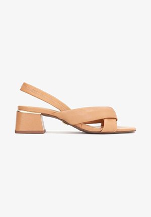 Sandale beige à talon bas avec une sangle devant le pied et des brides croisées rembourrées sur un fond blanc.