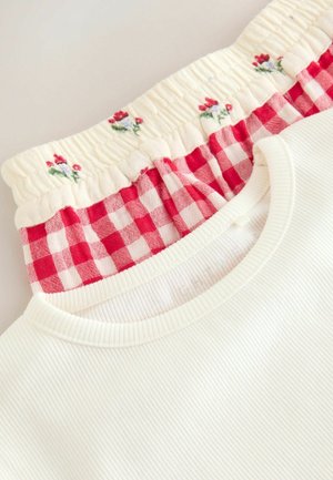 Valge ribastatud kangast top, millel on smockitud punase ja valge ruudulise krae ning millel on väiksed nõelutud lilled kreemivalge tausta peal.