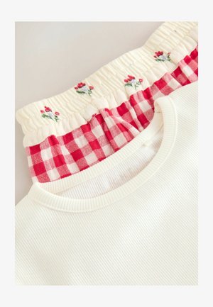 White ribbed fabric top with a smocked red and white gingham collar, featuring small embroidered flowers on a cream background.