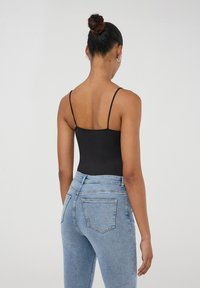 Bodycon con spalline nere abbinato a jeans blu chiaro a vita alta. Tessuto morbido, design aderente e stile classico a cinque tasche.