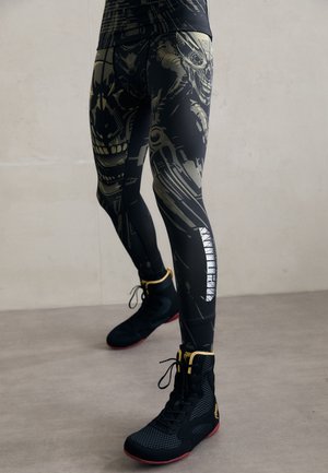 Legs wearing black athletic leggings with abstract skull designs and reflective text, paired with black and yellow high-top sneakers.
