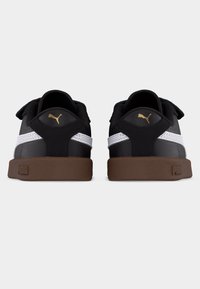 Ζευγάρι ασπρόμαυρα αθλητικά παπούτσια Puma με καφέ σόλες, εμφανιζόμενα από πίσω σε απλό ανοιχτό φόντο.