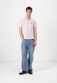 Polo shirt violet clair avec des manches courtes, deux boutons et un petit logo jaune. Assorti à un jean écourté bleu clair à jambes larges et des chaussures noires.
