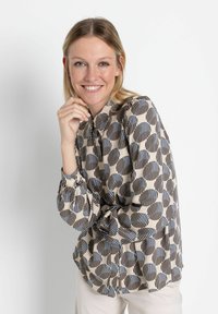 Langärmlige Bluse mit einem geometrischen Muster aus Kreisen und Streifen in Beige, Marineblau und Schwarz, mit einem Knopfkragen und gerafften Manschetten.