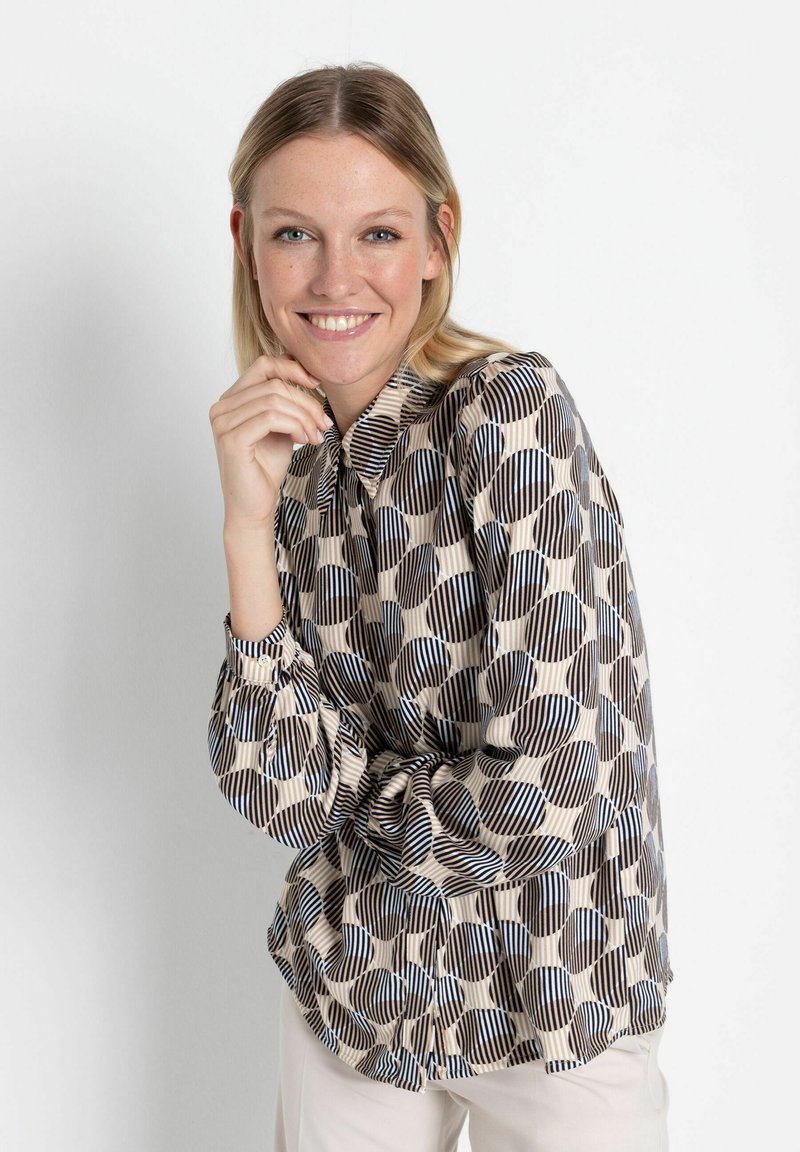 Langärmlige Bluse mit einem geometrischen Muster aus Kreisen und Streifen in Beige, Marineblau und Schwarz, mit einem Knopfkragen und gerafften Manschetten.