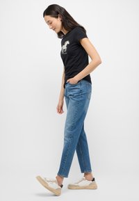 Czarny t-shirt z krótkim rękawem z białą grafiką konia, połączony z jasnoniebieskimi dżinsami o prostym kroju i beżowo-białymi trampkami.