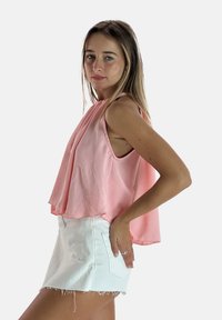 Top sin mangas de color rosa con frente drapeado, hecho de una tela ligera, combinado con pantalones cortos de mezclilla blancos de cintura alta. Dobladillo texturizado y bolsillos laterales.